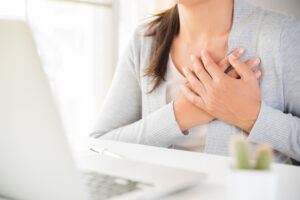 Woman holding hand over heart sitting at her office desk taking a breath